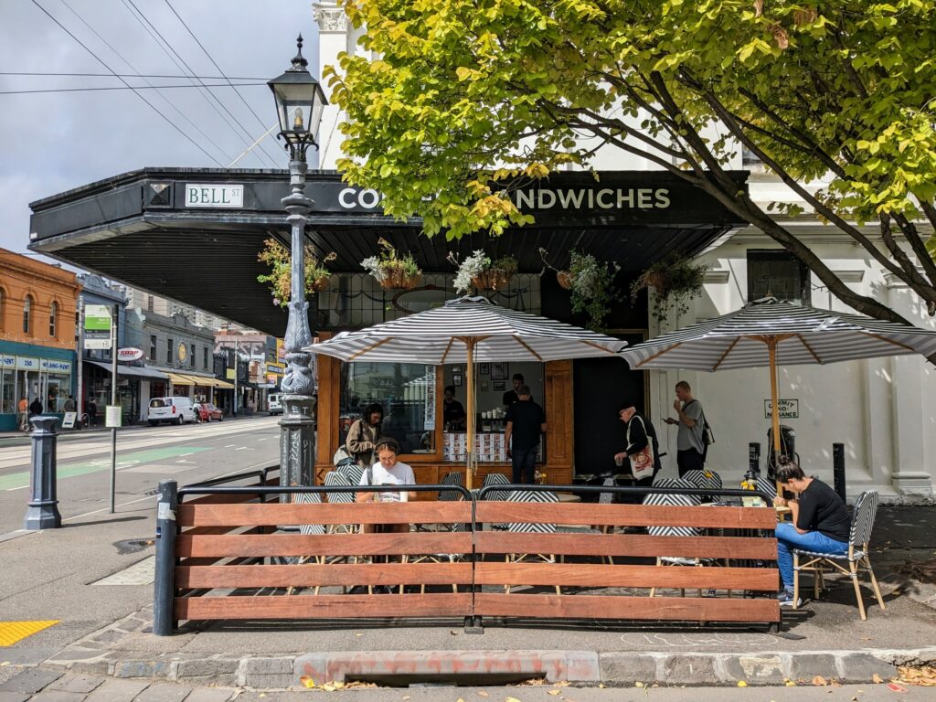 Exterior view of Bell Street Coffee Window in Fitzroy, Melbourne, with tables and chairs under umbrellas outside