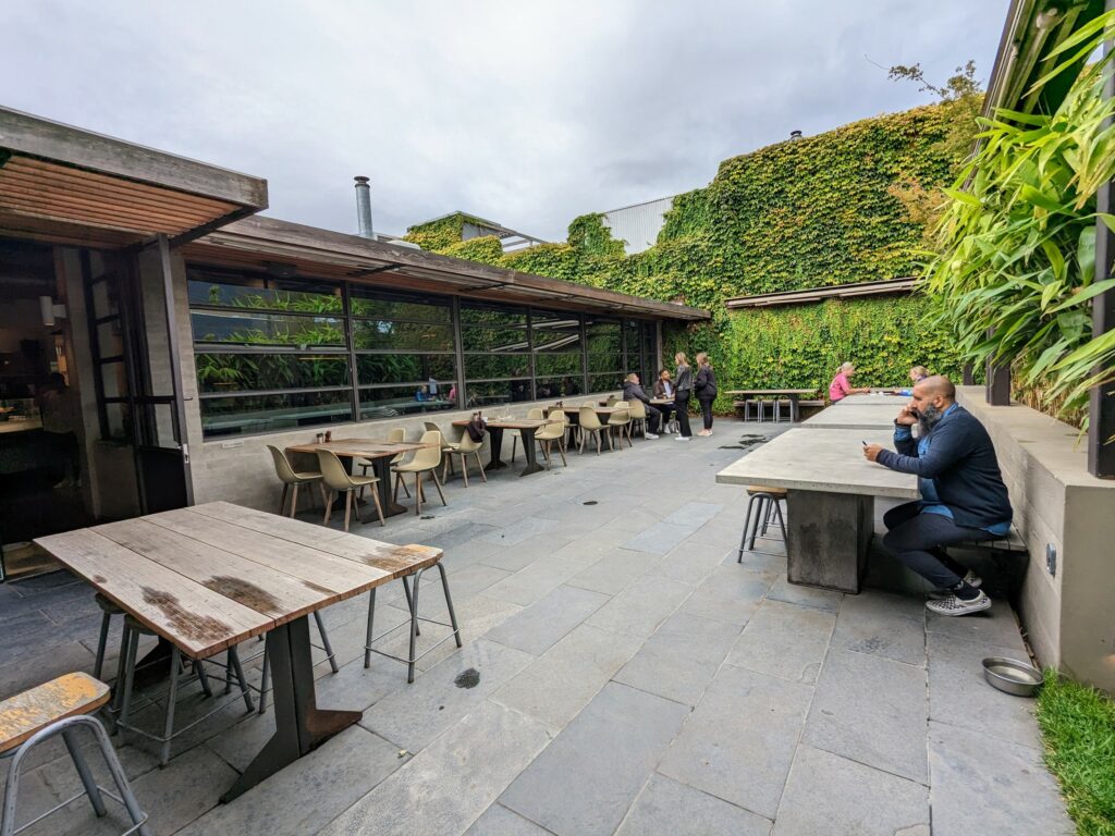 Cafe courtyard with several tables and chairs, and living wall at rear.