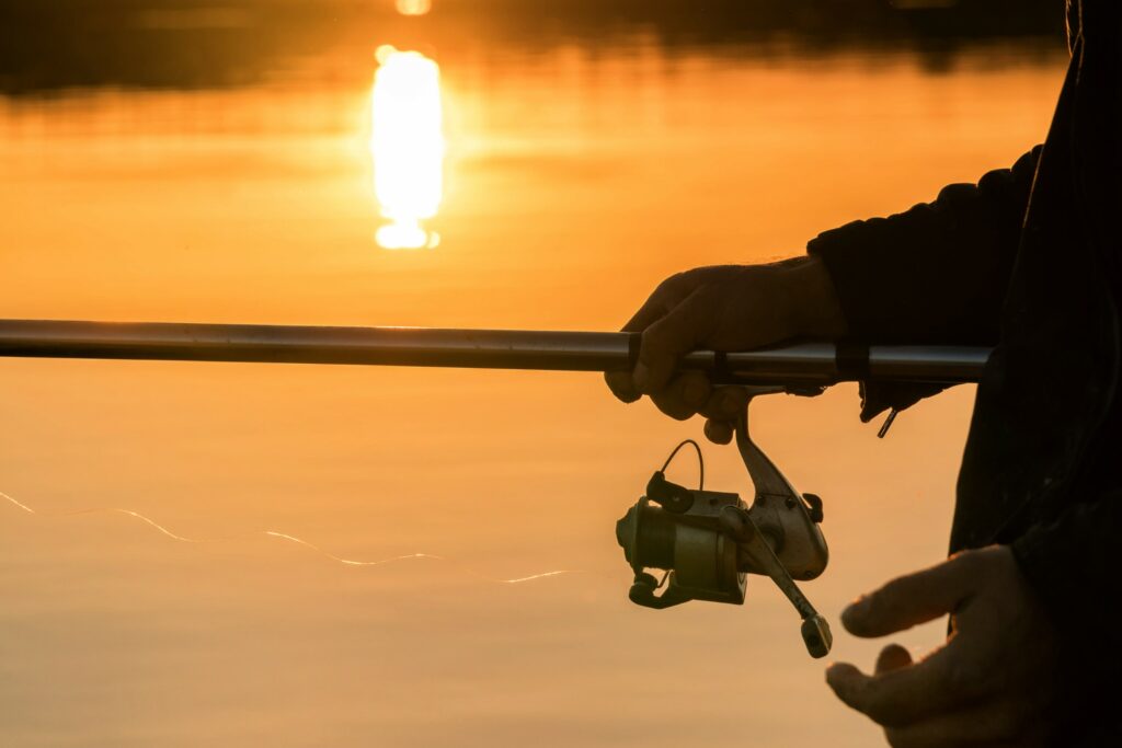 Close up of person holding fishing rod with golden light on water in background
