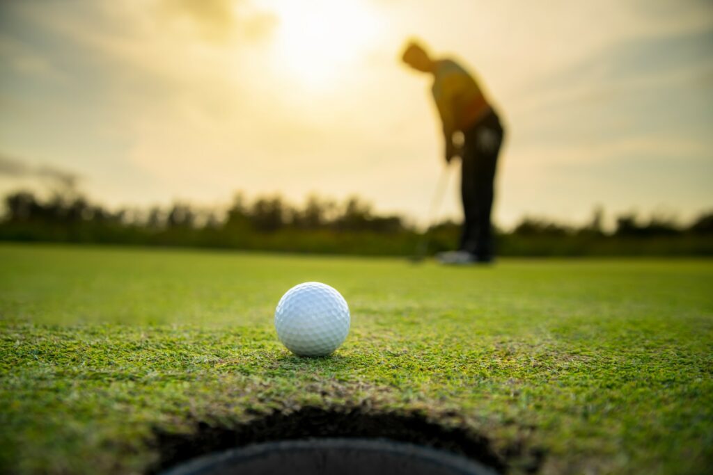 Golf ball almost in the hole, with blurred person standing behind with putter in hand