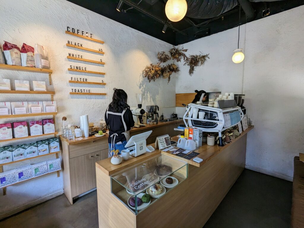 Inside of Calēre Coffee in Fitzroy, Melbourne, showing counter, coffee machine, food, and bags of coffee on shelves