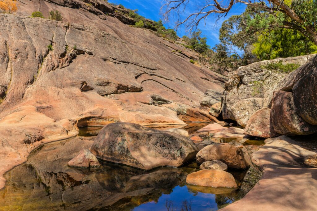 Shallow natural pool surrounded by sloping rocks with blue sky and trees in background