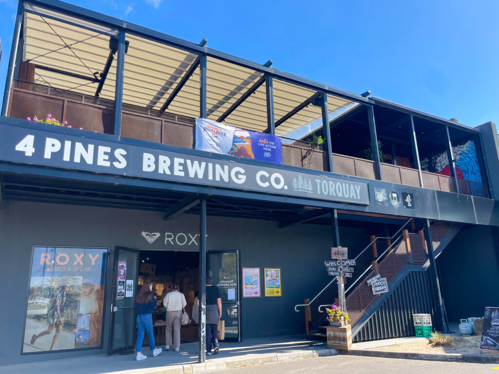 Two-story building with Roxy branding on the lower level and 4 Pines Brewing Co. on the upper level. External stairs lead from the ground to the upper level.