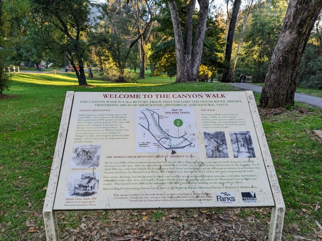 Information board giving the history and track information for the Bright Canyon Walk. Trees and paved path in the background.
