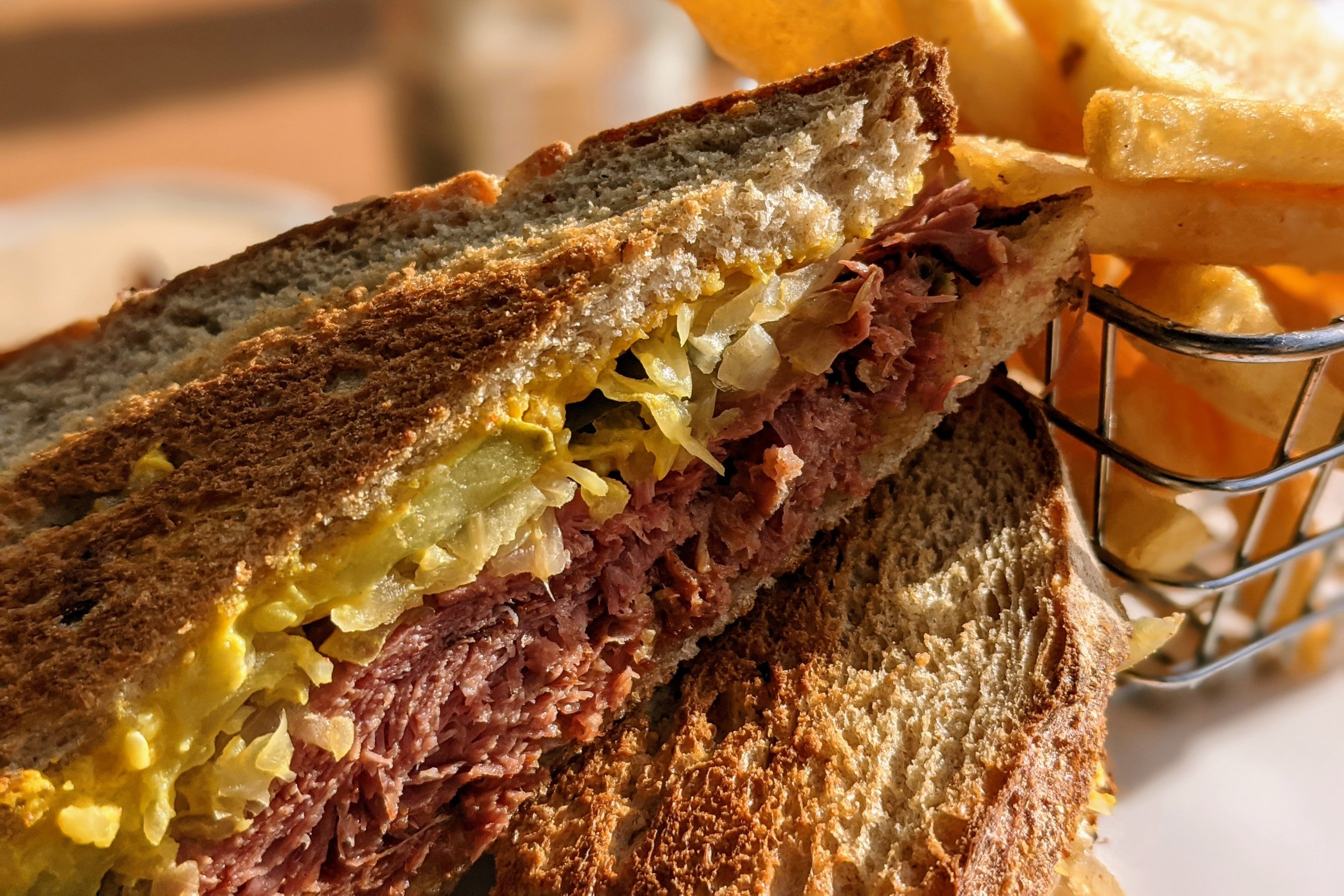Closeup photo of sandwich with metal basket of chips in the background