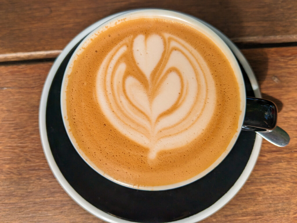 An overhead view of a mug of coffee with a latte art design of a heart and flower