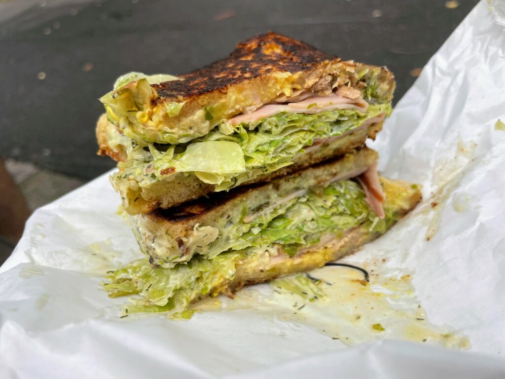 Cubano toasted sandwich on white wrapper, with paved path in the background