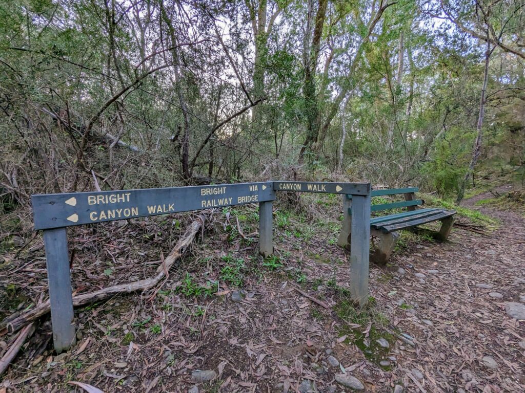 Direction signposts alongside wooden bench and walking path, pointing to the Canyon Walk in two directions, and Bright via the railway bridge in the other