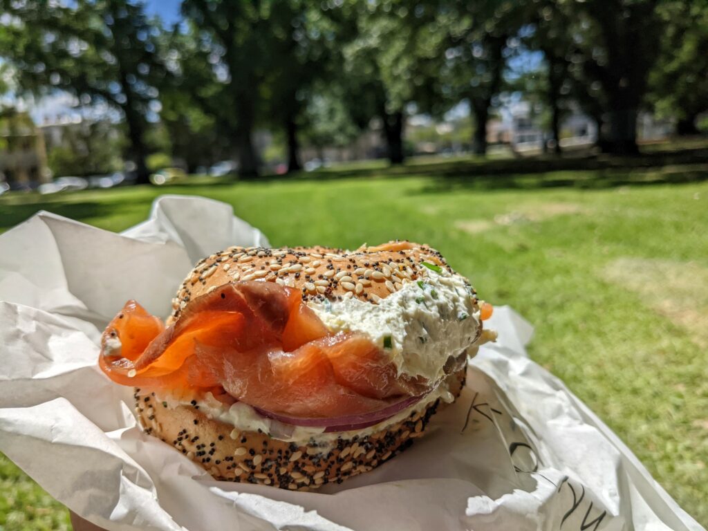 Salmon and cream cheese bagel on a paper wrapper, with blurred grass and trees in background