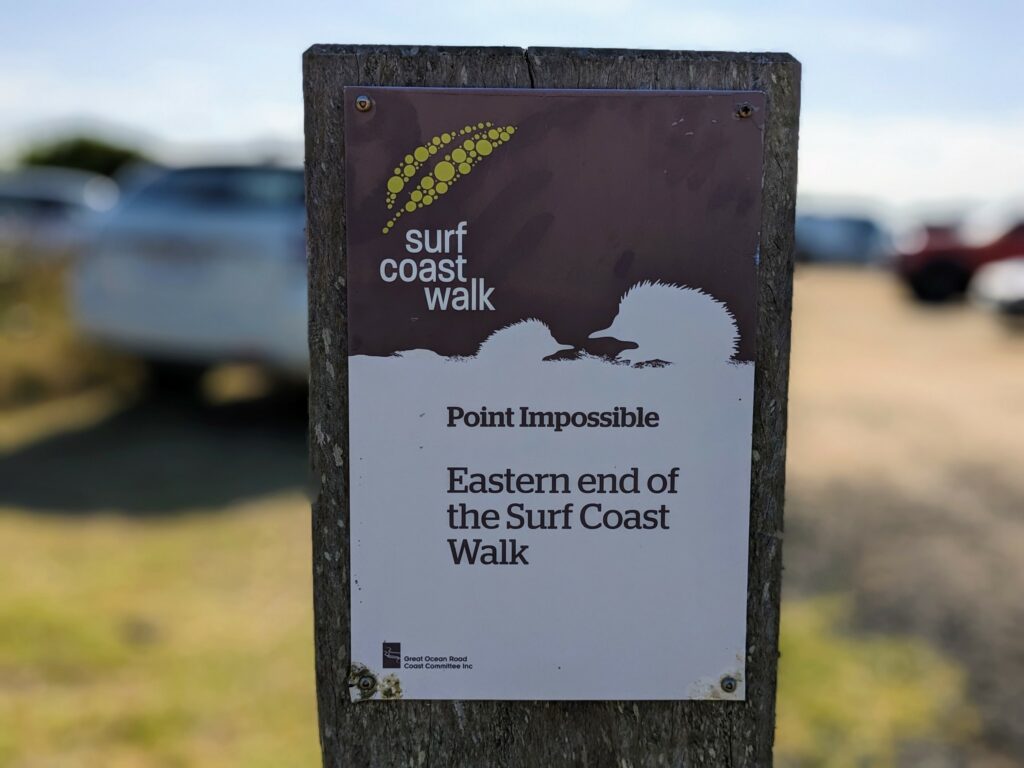 Sign for Point Impossible at the eastern end of the Surf Coast Walk, with blurred parking lot in the background