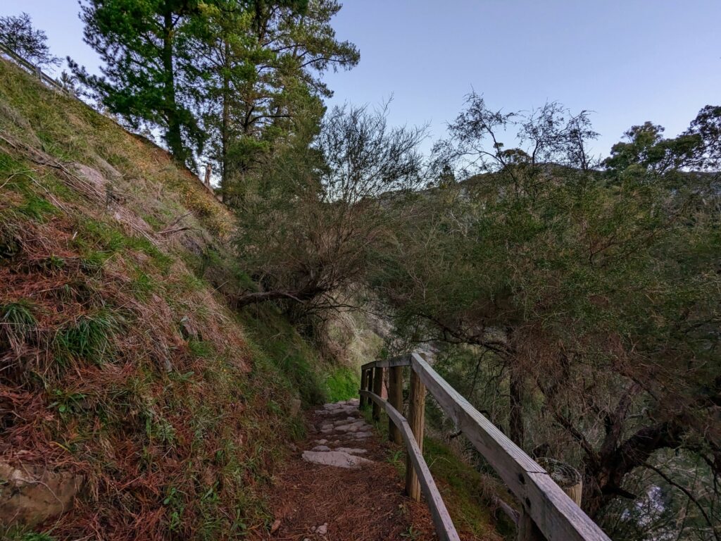 Stone steps descending on a narrow trail, with hillside to the left and a wooden fence to the right