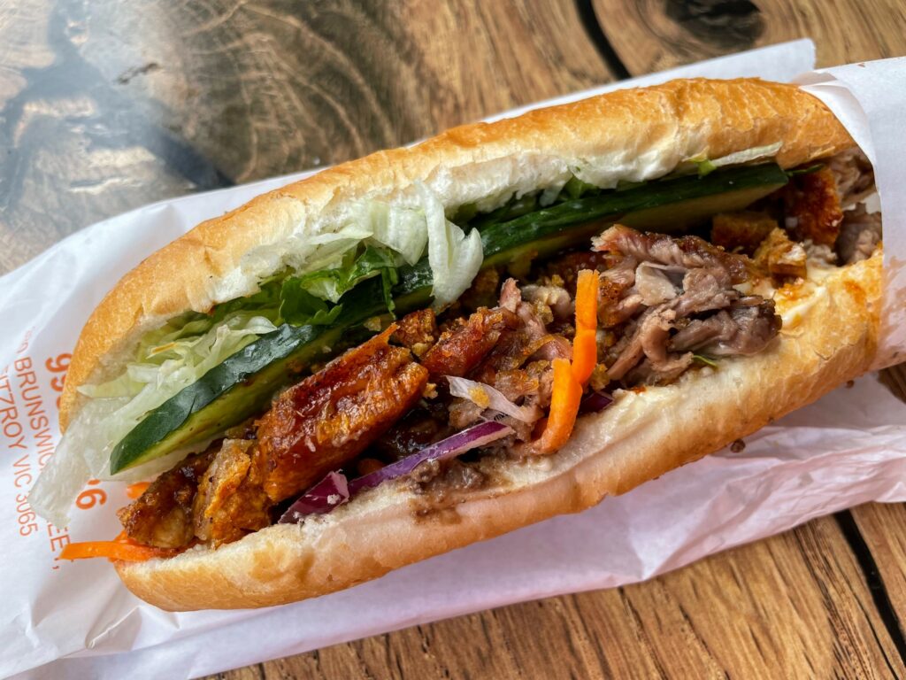 Banh mi with crispy pork and vegetables inside, on wooden table