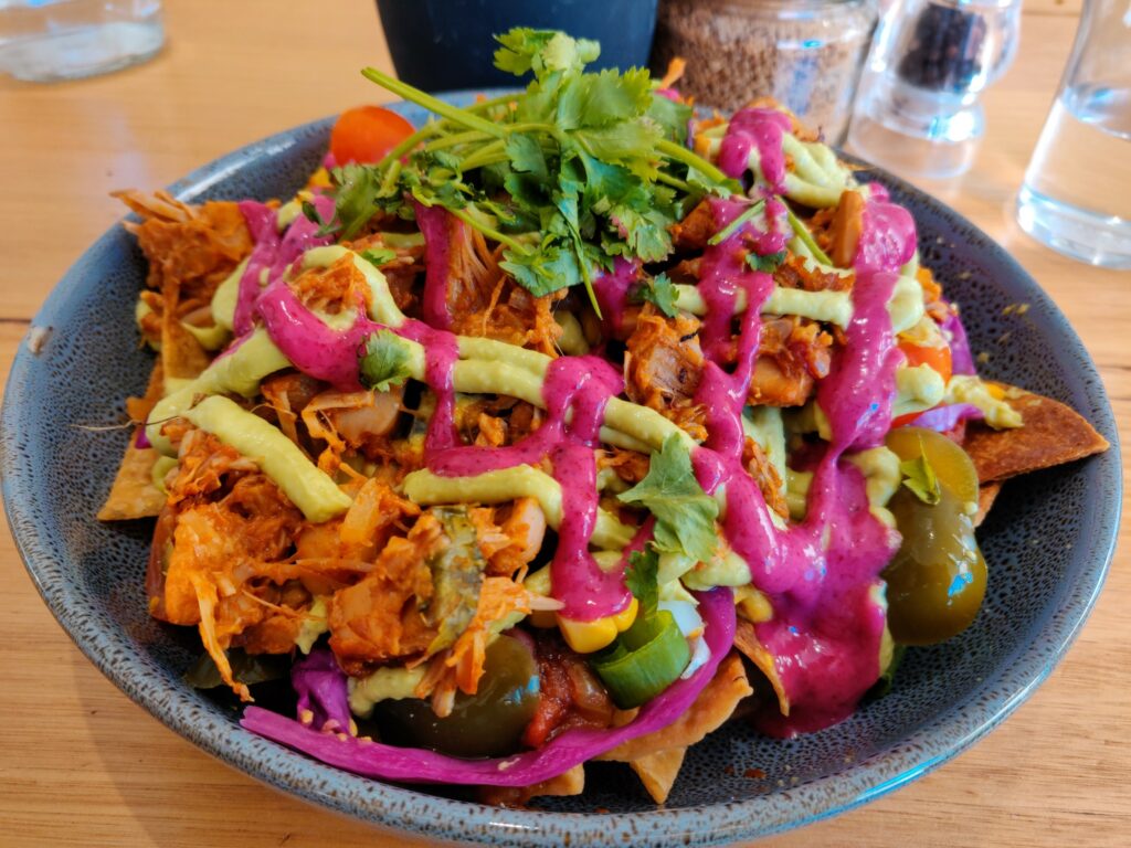 Bowl of nachos with plant-based ingredients and a vibrant crimson sauce on a wooden table.