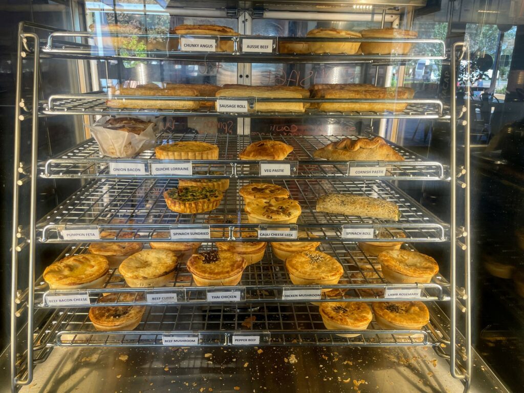 Wide range of pies, pastries, sausage rolls, and quiches inside a pie warmer.