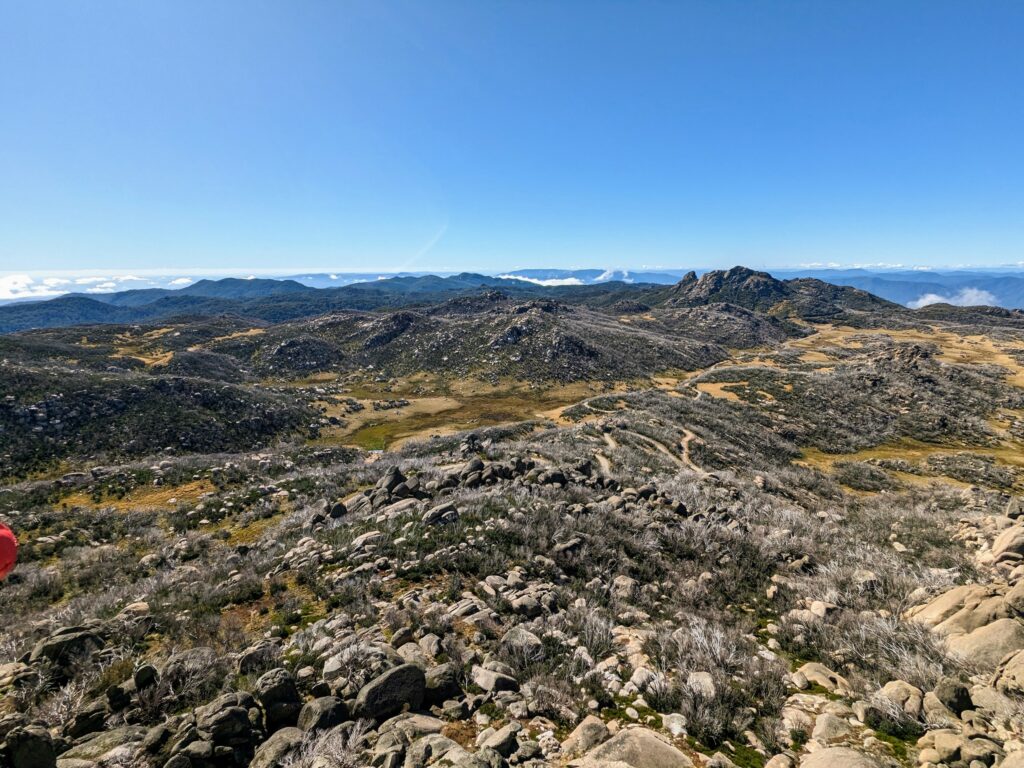 Expansive view out over fields of granite boulders, with a winding dirt road snaking through it into the distance. Hills and mountains visible all the way to the horizon.