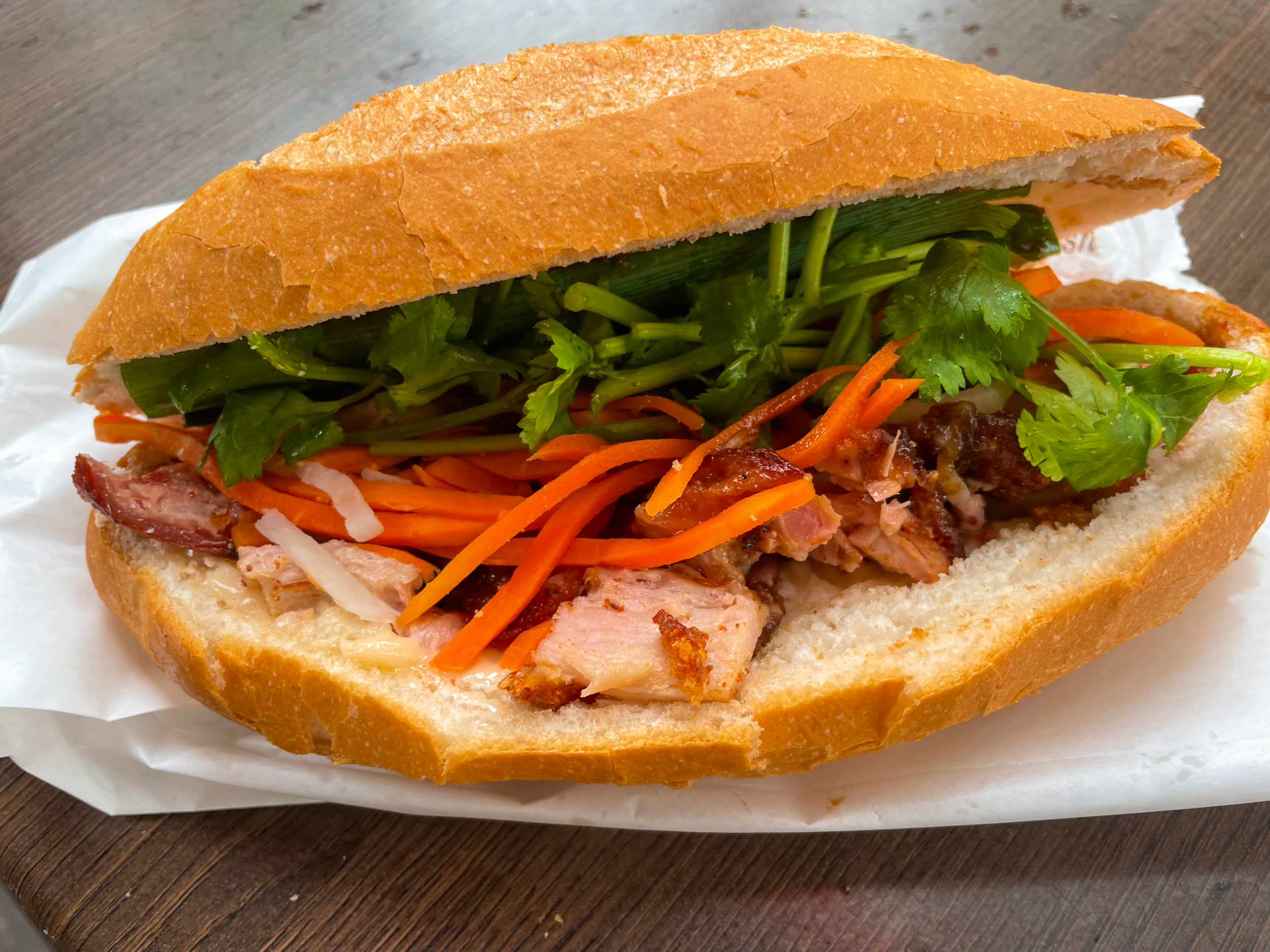 Banh mi bread roll with pork, coriander, and other fillings inside. Sitting on paper bag