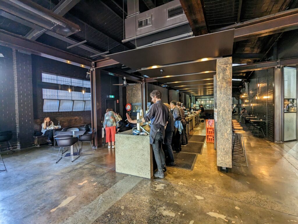 Interior of Code Black Coffee, with dark,  industrial brick and stone design. Staff members standing behind a long counter making coffee. A few tables and chairs visible.