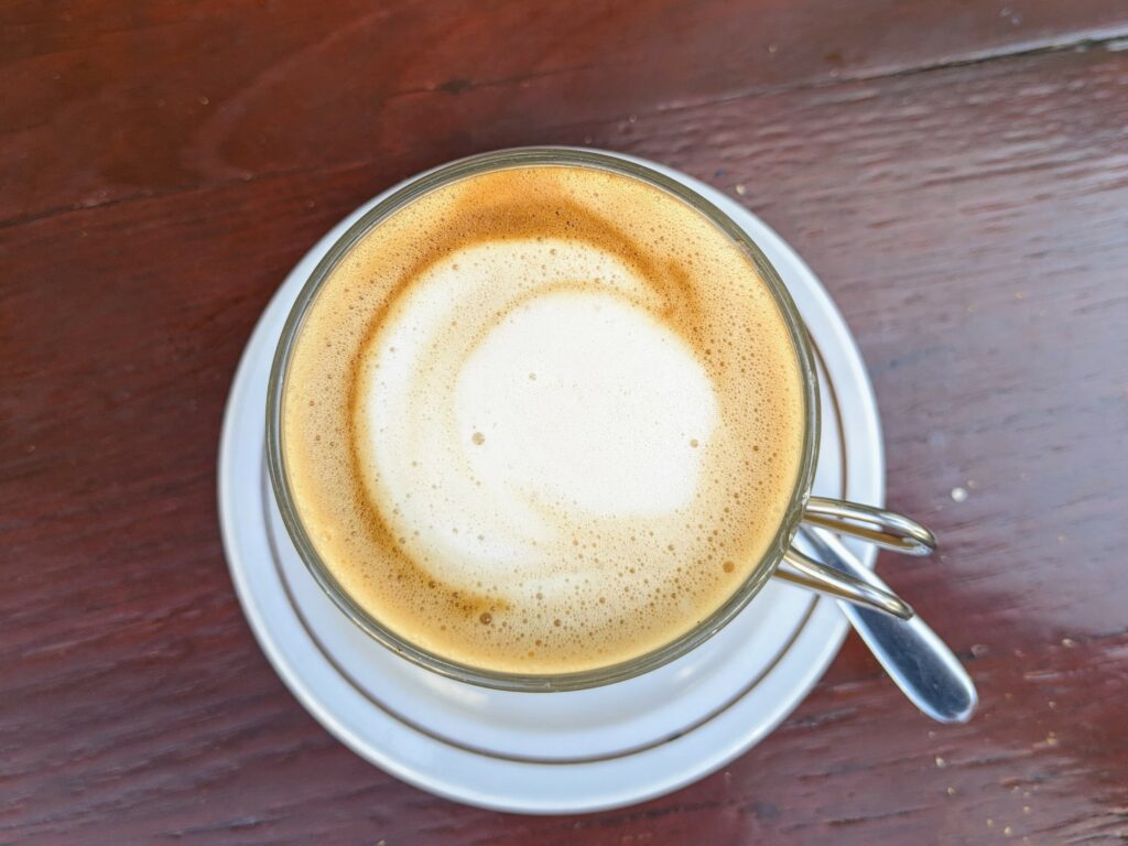 Overhead view of latte in a glass, sitting on a saucer on a painted wooden table