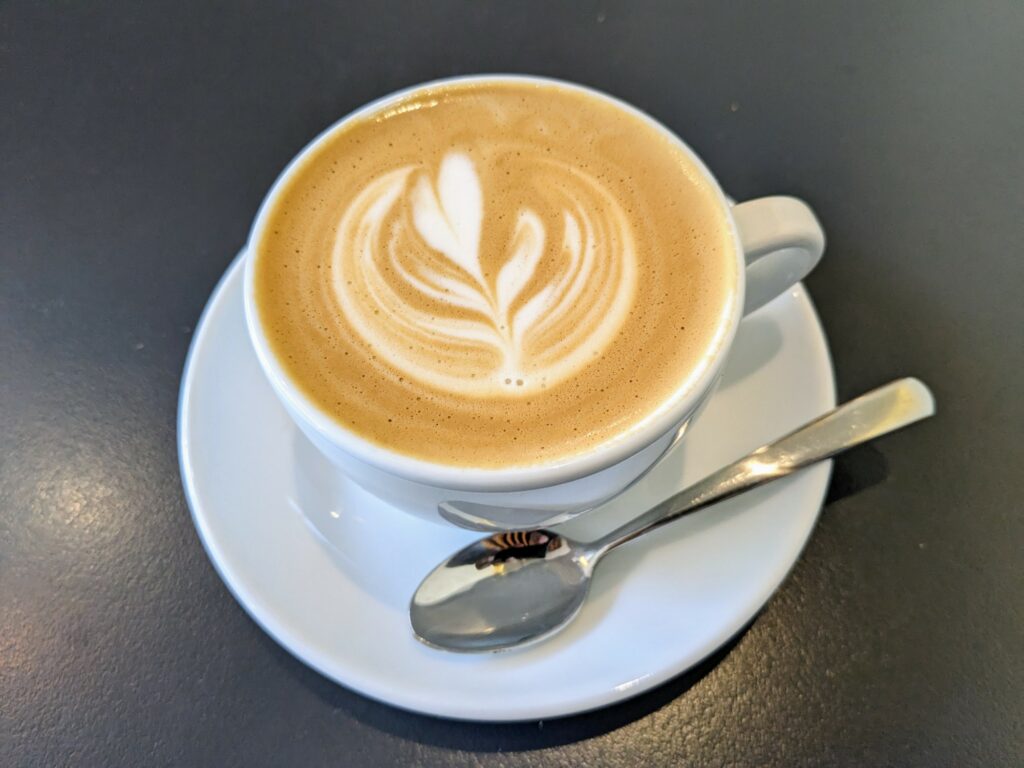 Overhead view of coffee with latte art, in a white cup on a white saucer on a black table.