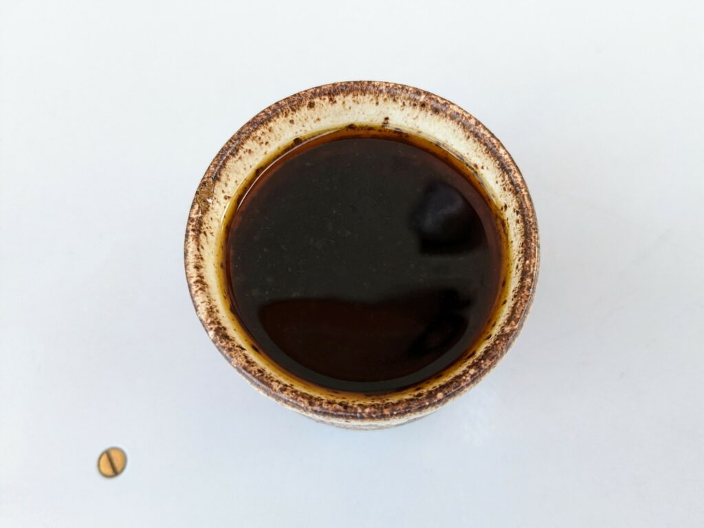 Overhead view of black coffee in a patterned ceramic cup, on a white table. One small screwhead visible alongside.