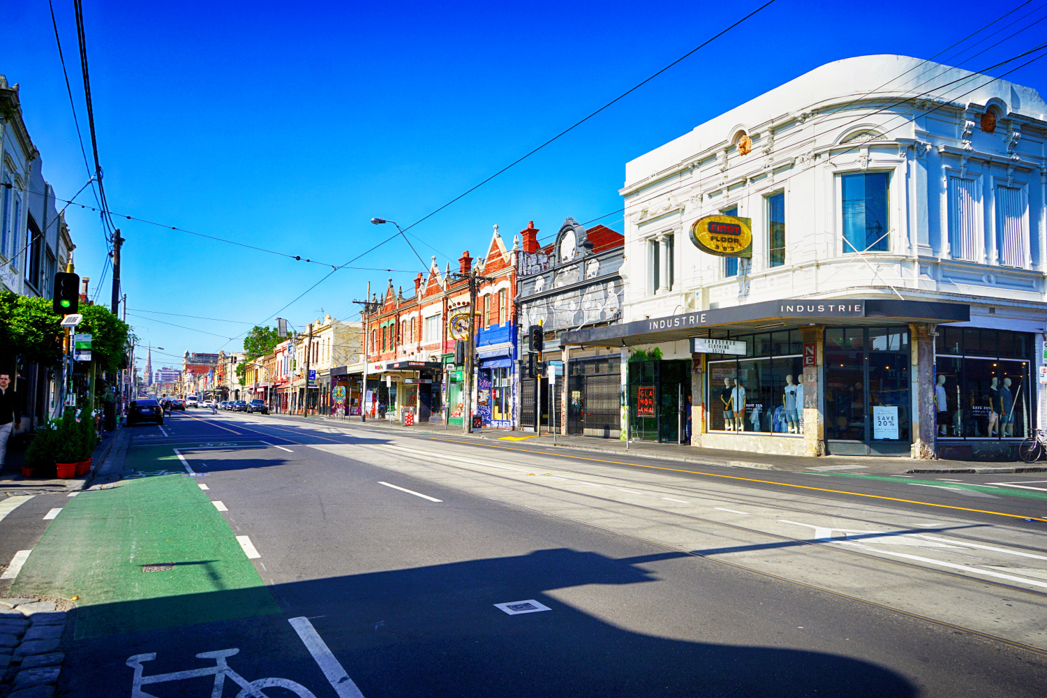 A panoramic view of Brunswick Street on an abnormally quiet day. The sky is blue, the road is empty, and the Victorian architecture is encased in street art and graffiti