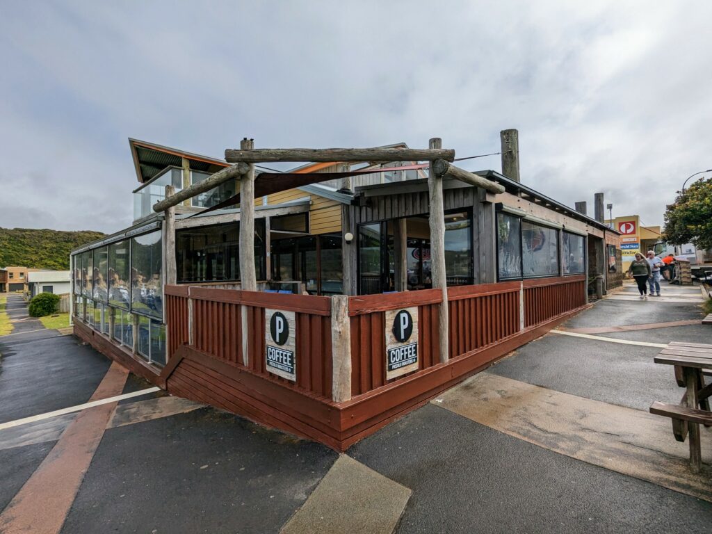 Exterior of 12 Rocks Beach Bar and Cafe in Port Campbell. Wet footpath, and sun is just starting to break through the clouds.