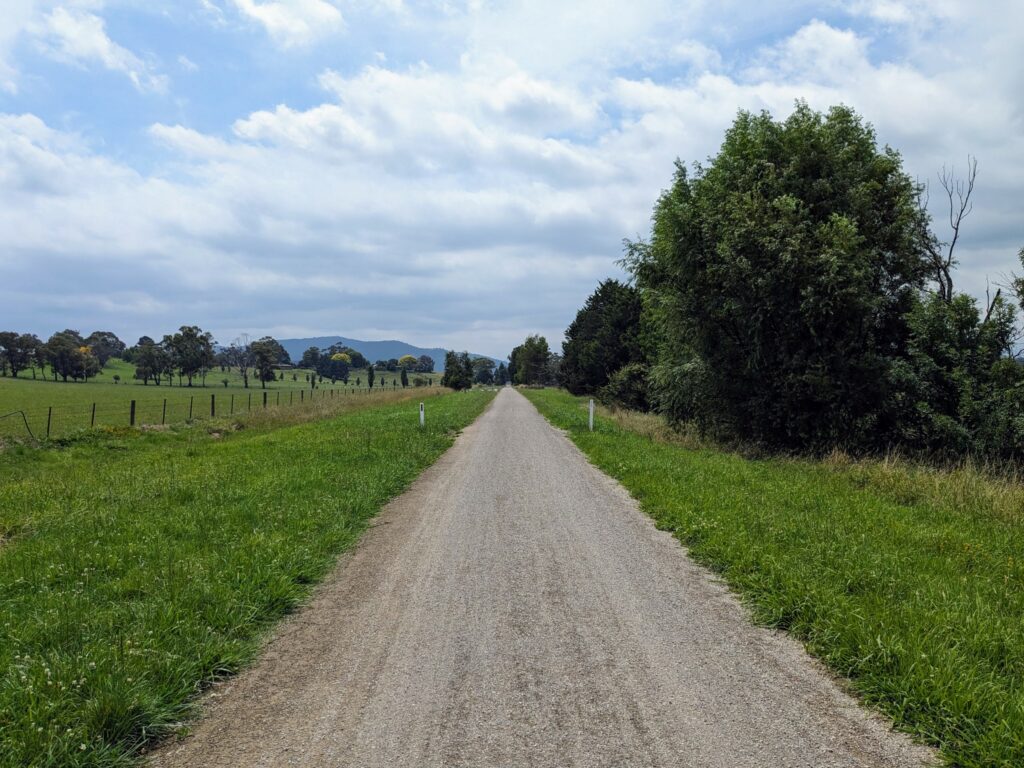 Long straight stretch of gravel hiking/biking trail, with grass and trees on both sides.